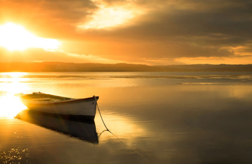 A peaceful and serene looking boat sits docked on the lake in the glowing afternoon sunlight.