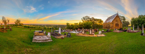 A cute little church and graveyard overlooking a valley at sunset.