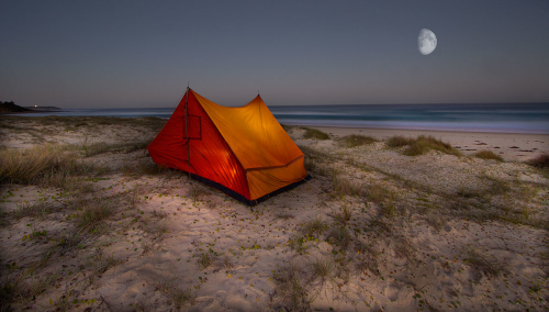 An Illuminated tent sits on sand dunes overlooking the ocean on the South Coast of NSW.