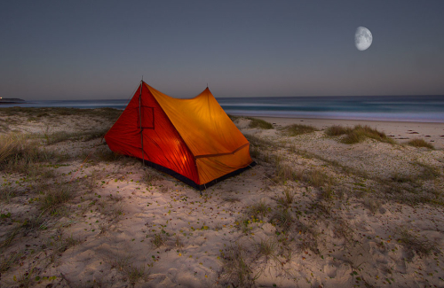 An Illuminated tent sits on sand dunes overlooking the ocean on the South Coast of NSW.