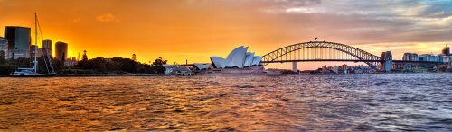 The orange afterglow of sunset lingers over the Opera House and Sydney Harbour Bridge, as a lone yacht bobs nearby.